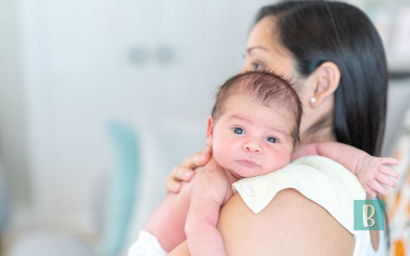 Recém-nascido no colo da mãe, com olhar atento e apoiado em uma fralda de pano